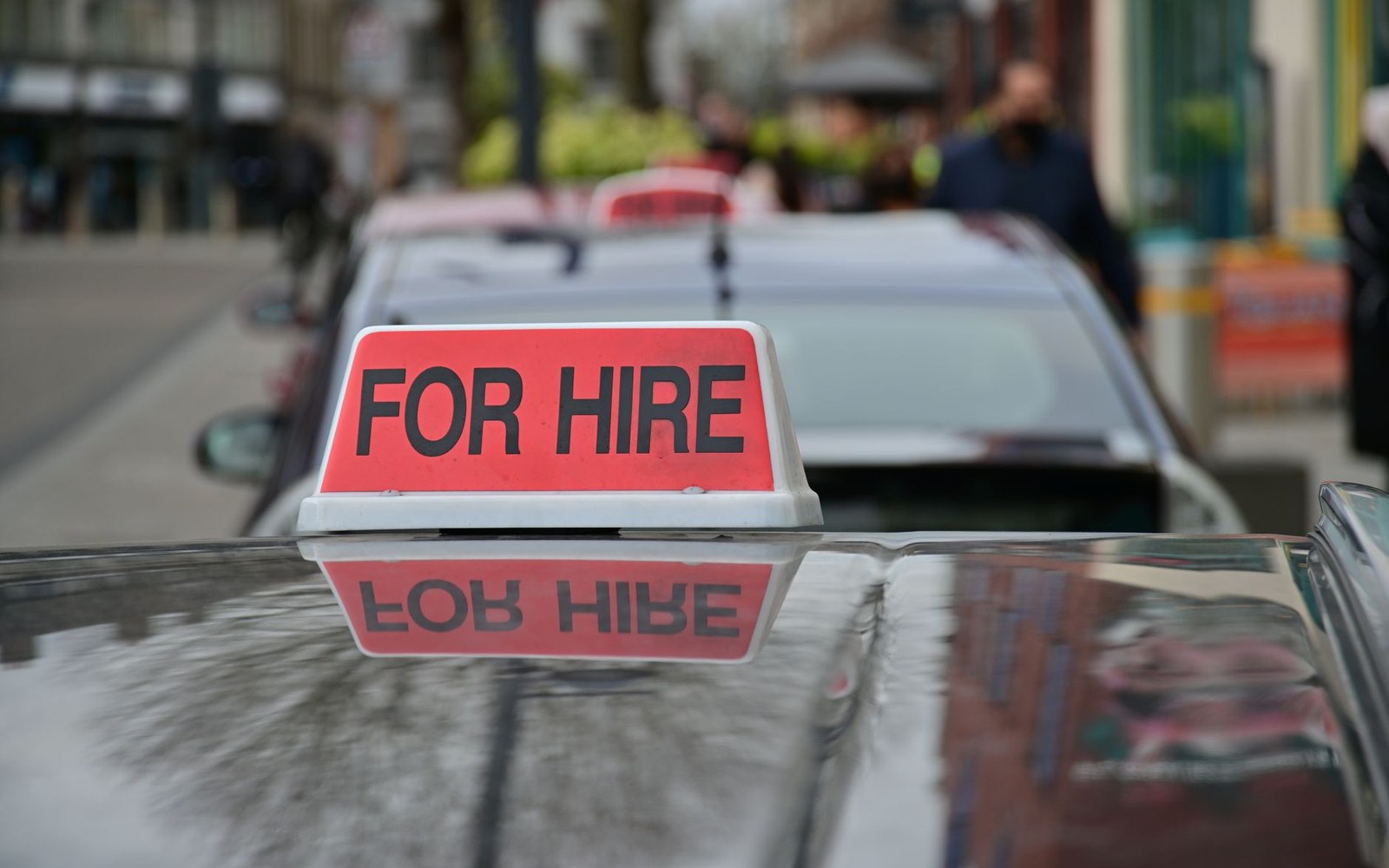 A red "for hire" sign mounted on a taxi's roof along a city street