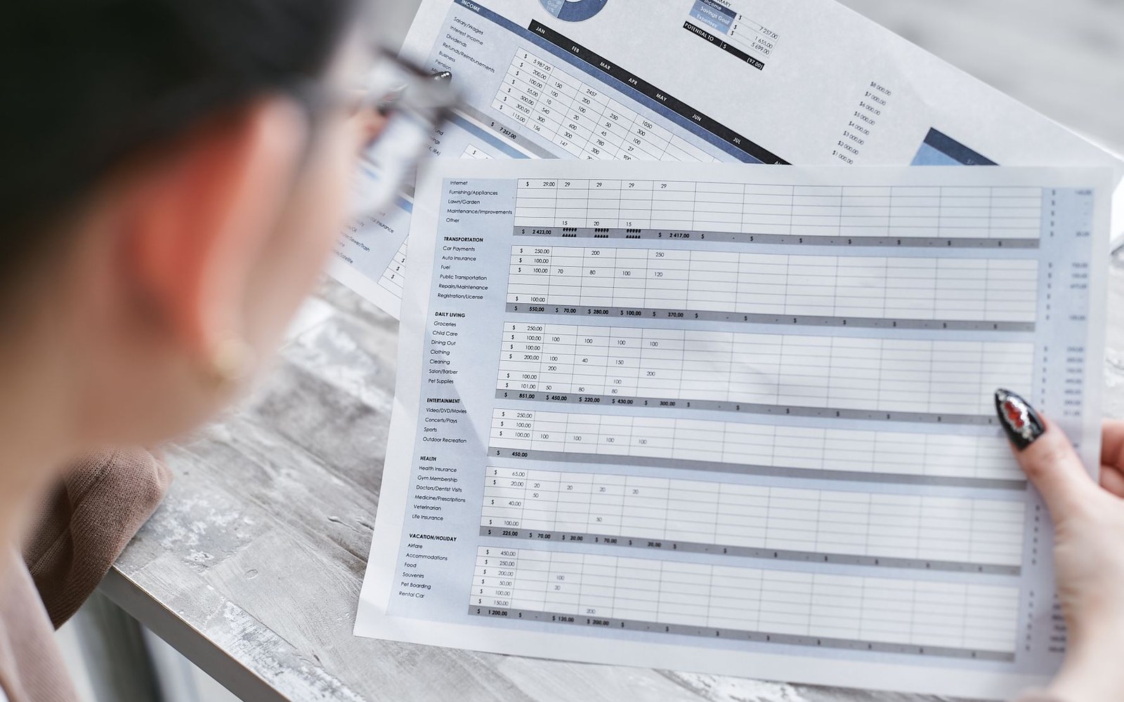 Person holding printed budget spreadsheets with rows of expense categories and dollar figures